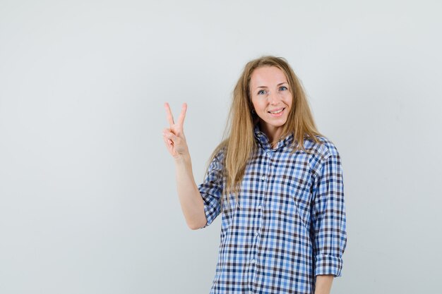 Blonde woman in shirt showing victory sign and looking jolly ,