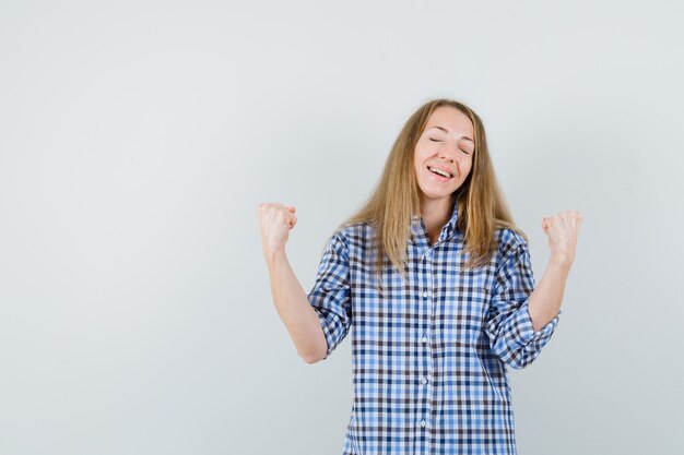 Blonde woman in shirt showing winner gesture and looking lucky ,