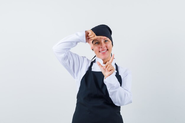 Бесплатное фото Блондинка женщина показывает жест кадра руками в черной форме повара и выглядит красиво, вид спереди.