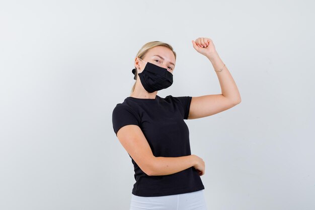 Blonde woman showing muscles of arm in black t-shirt, white pants