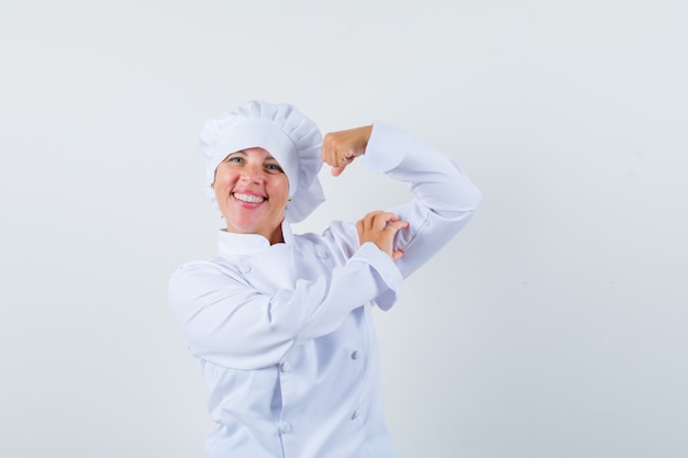 Blonde woman showing muscles in white cook uniform and looking pretty.