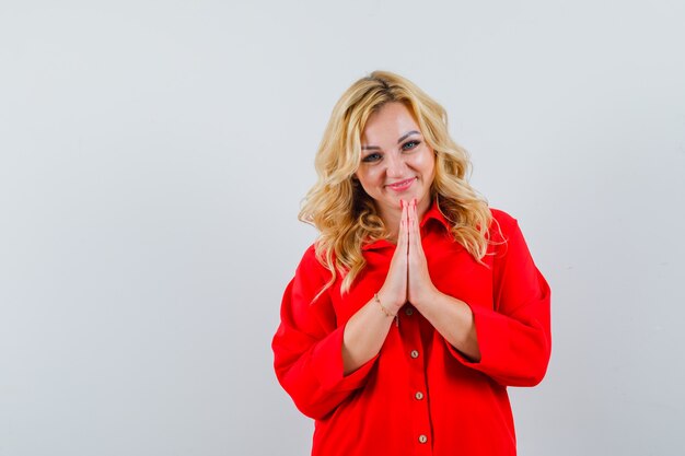 Free photo blonde woman showing namaste gesture in red blouse and looking happy.