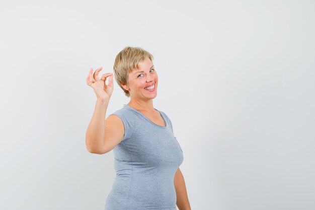 Blonde woman showing okay sign and smiling in light blue t-shirt and looking optimistic , front view.