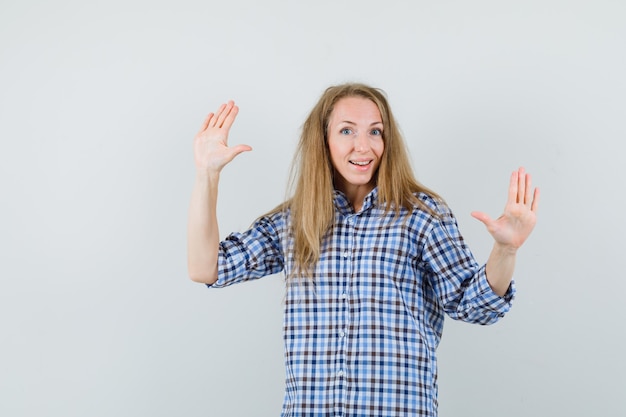 Blonde woman showing palms in shirt and looking cheerful ,