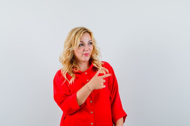 Blonde woman showing peace sign in red blouse and looking happy.