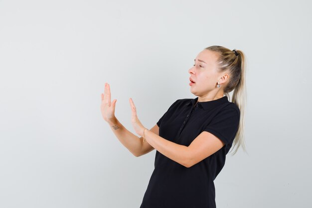 Blonde woman showing refuse or deny gesture in black t-shirt and looking frightened