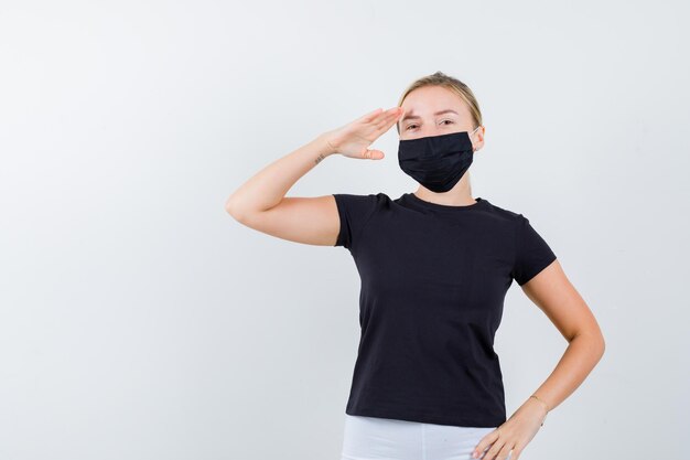 Blonde woman showing salute gesture, holding hand on waist in black t-shirt