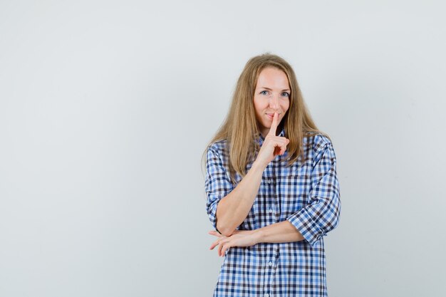 Blonde woman showing silence gesture in shirt and looking jolly.