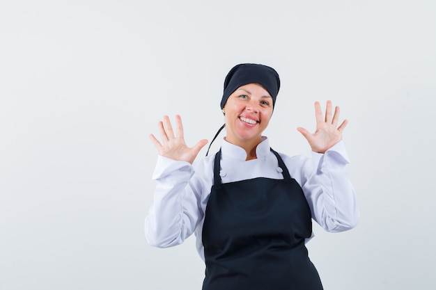 Blonde woman showing stop gestures in black cook uniform and looking pretty.