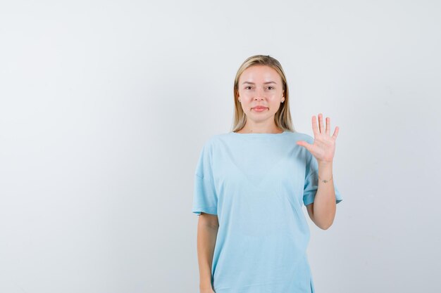 青いTシャツで一時停止の標識を示して、かわいく見えるブロンドの女性