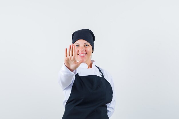 Blonde woman showing stop sign with hand in black cook uniform and looking pretty