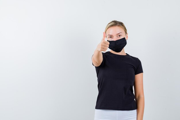 Blonde woman showing thumb up in black t-shirt, white pants