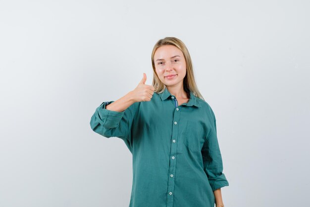 Blonde woman showing thumb up in green shirt and looking cheerful.