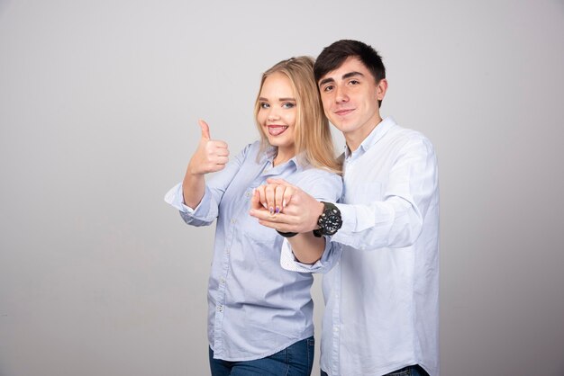 Blonde woman showing thumb up while holding her boyfriend's hand .