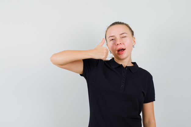 Blonde woman showing thumbs up and winking in black t-shirt and looking happy