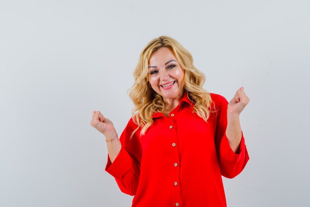 Blonde woman showing winner gesture in red blouse and looking happy ,