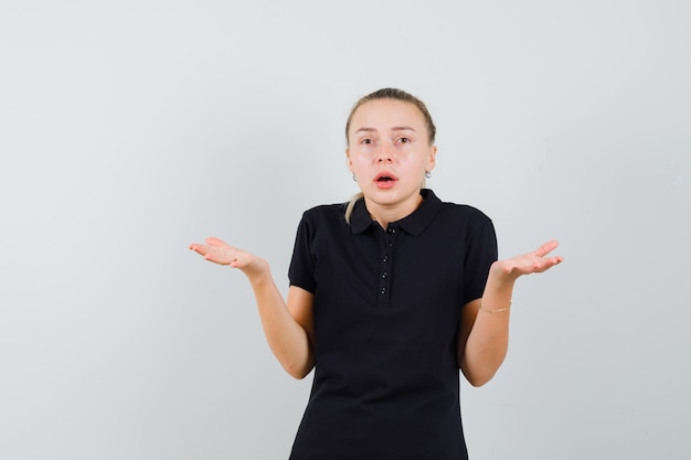 Blonde woman shrugging her shoulders in black t-shirt and looking confused