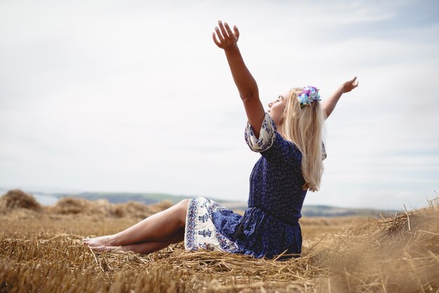 Blonde woman sitting in field with her arms raised