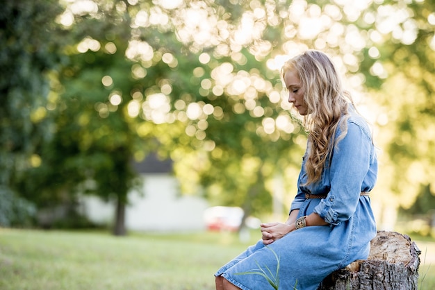 Блондинка сидит на пне и молится в саду под солнечным светом
