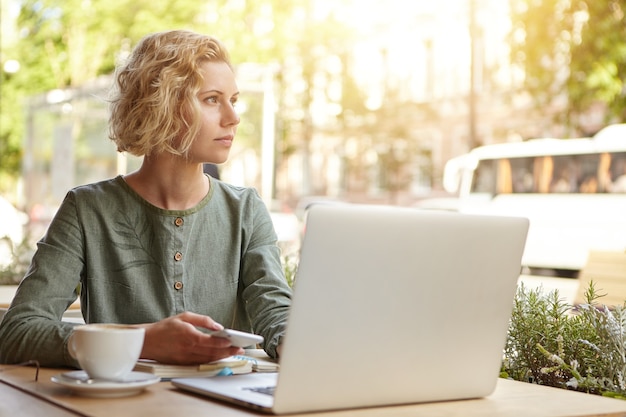 Donna bionda che si siede con il computer portatile nella caffetteria