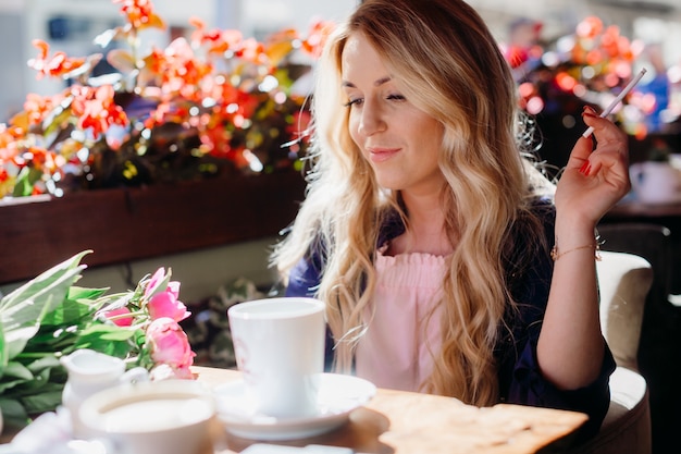 Blonde woman smokes a cigar drinking coffee in the cafe