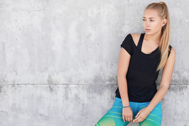 Blonde woman in sportswear near concrete wall