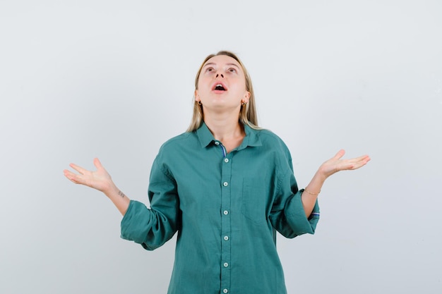 Blonde woman spreading palms aside while looking up in shirt, jacket and looking grateful.