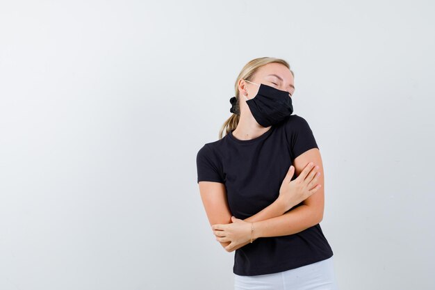 Blonde woman standing arms crossed, hugging herself while posing in black t-shirt