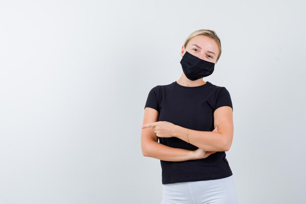 Blonde woman standing arms crossed, pointing left with index finger in black t-shirt