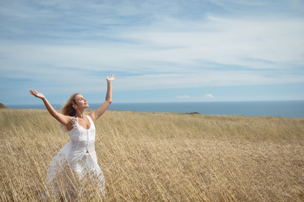 Free photo blonde woman standing in field with arms raised