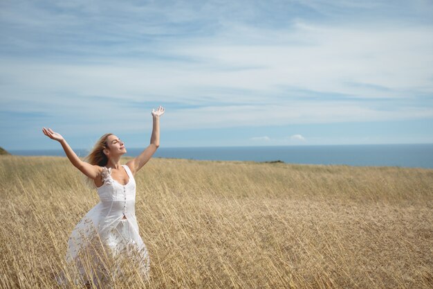 Blonde woman standing in field with arms raised