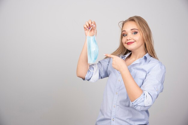 blonde woman standing and pointing at medical face mask .