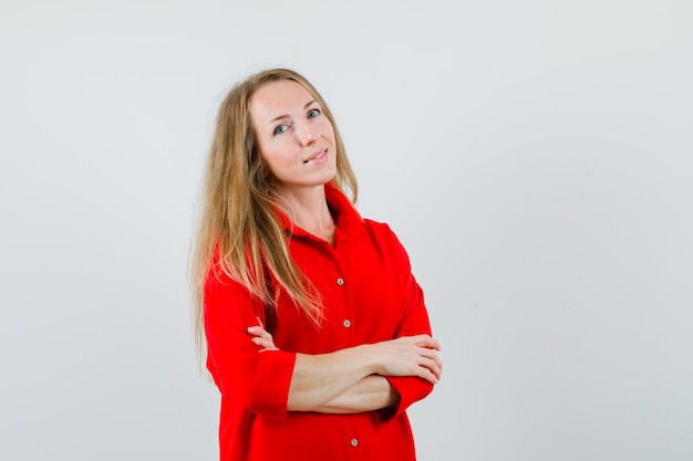 Blonde woman standing with crossed arms in red shirt and looking confident ,