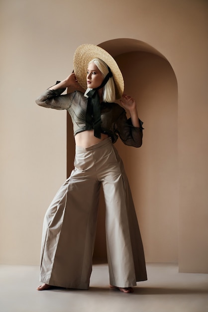 Free photo blonde woman in straw hat standing near wall with barefoot