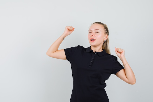 黒のtシャツでストレッチとあくびをし、疲れているように見えるブロンドの女性