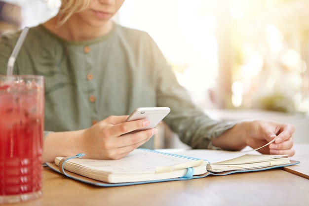 Foto gratuita donna bionda che studia nella caffetteria sorseggiando un drink