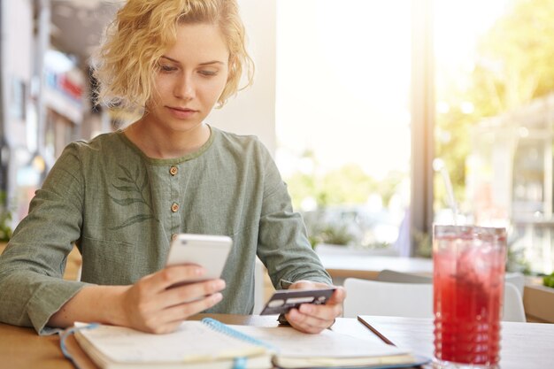 ドリンクを飲みながらカフェで勉強しているブロンドの女性