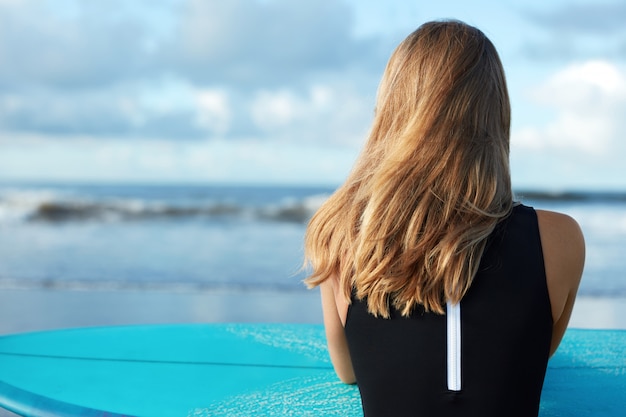 Donna bionda in costume da bagno con tavola da surf sulla spiaggia
