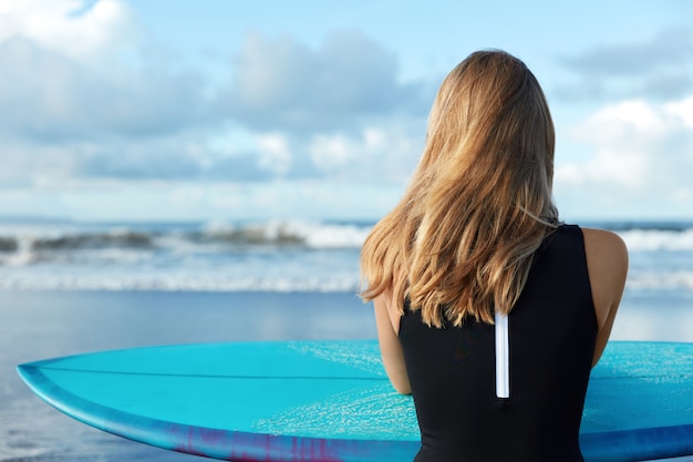 Foto gratuita donna bionda in costume da bagno con tavola da surf sulla spiaggia