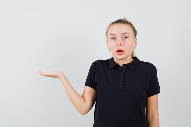 Blonde woman tipping her hand in black t-shirt and looking surprised