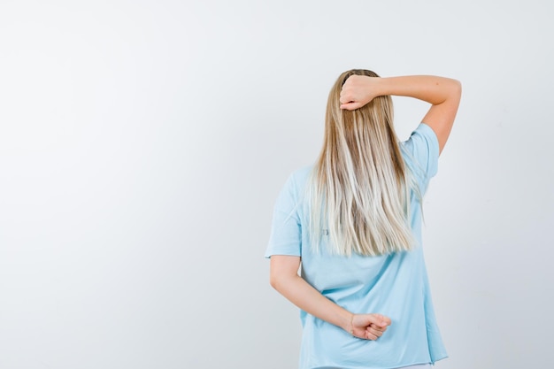 Blonde woman turning back, clenching fists in blue t-shirt and looking cute