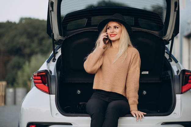 Бесплатное фото Блондинка женщина с помощью телефона и сидя в багажнике автомобиля