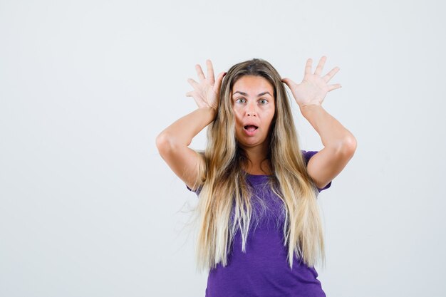 blonde woman in violet t-shirt doing funny gesture with hands and looking amused , front view.