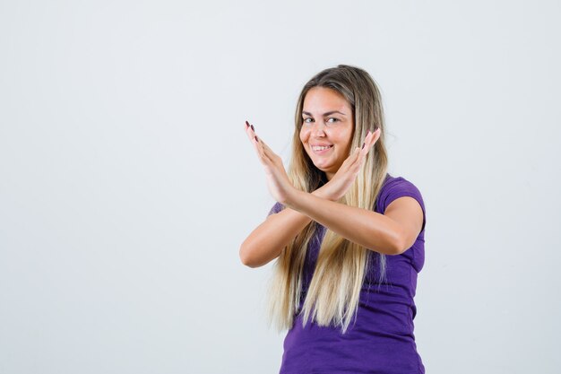 блондинка в фиолетовой футболке показывает жест стоп и выглядит счастливой, вид спереди.
