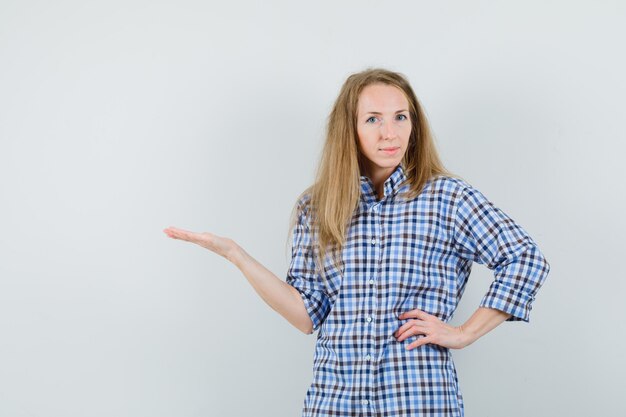 Blonde woman welcoming or showing something in shirt and looking confident.