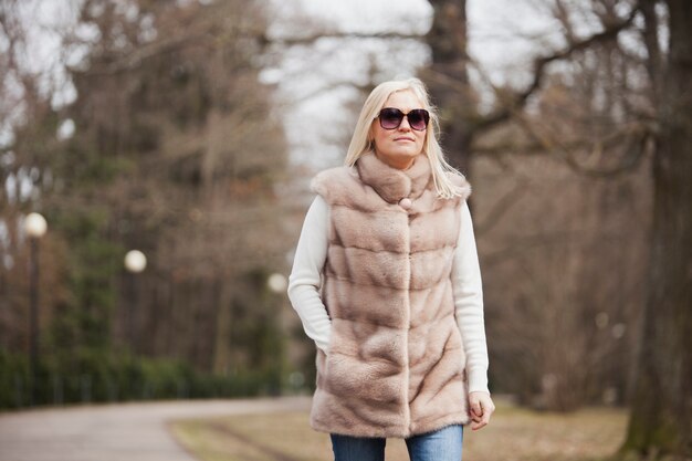 Donna bionda con gli occhiali da sole che camminano nel parco