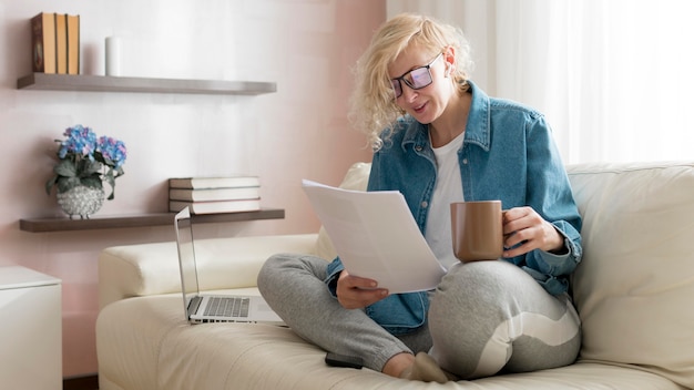 Blonde woman working on couch and drinking coffee