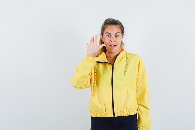 Blonde woman in yellow bomber jacket and black pants showing stop sign and looking happy