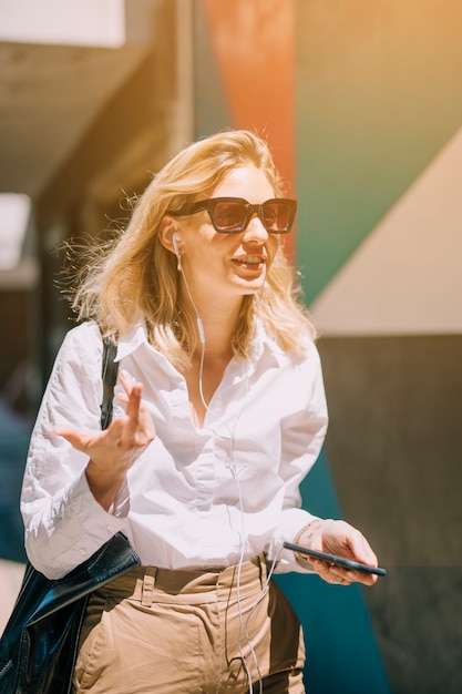 Blonde young business woman in sunlight listening music on cellphone gesturing