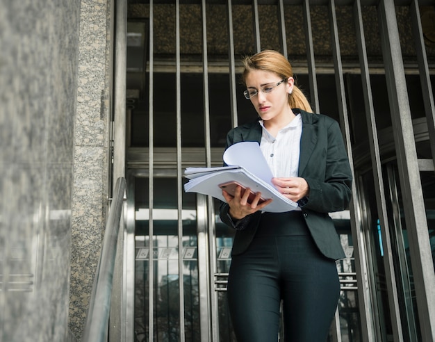 Free photo blonde young businesswoman standing against the entrance checking document